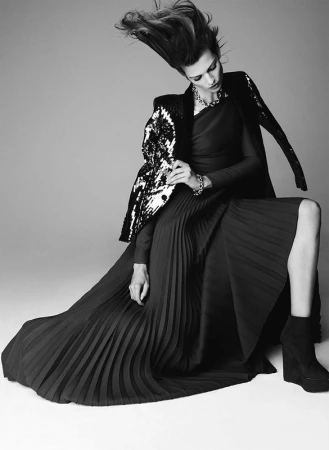 Monochrome fashion portrait of a model with hair caught in motion wearing a pleated dress and sequined jacket