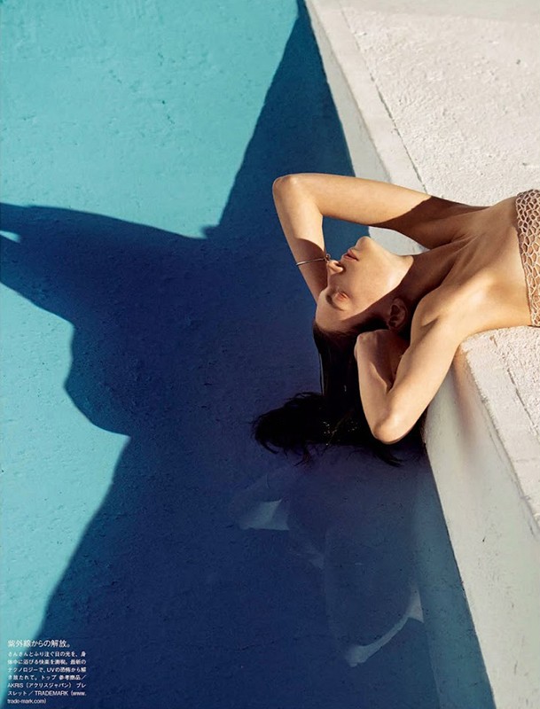 Woman relaxing near pool with blue water and geometric shadows. Summer fashion shot with natural light and dark hair.