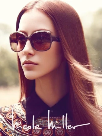 Close-up portrait of a woman wearing oversized brown sunglasses and a patterned top with hair styling by Tuan Anh Tran.