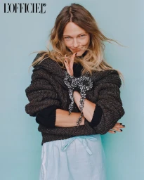 Model with blonde hair styling by Tuan Anh Tran wearing a textured dark brown sweater and light blue skirt against a pale background