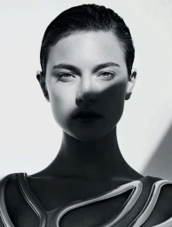 Close-up monochrome portrait of a woman with slicked-back dark hair and dramatic diagonal shadow across her face.