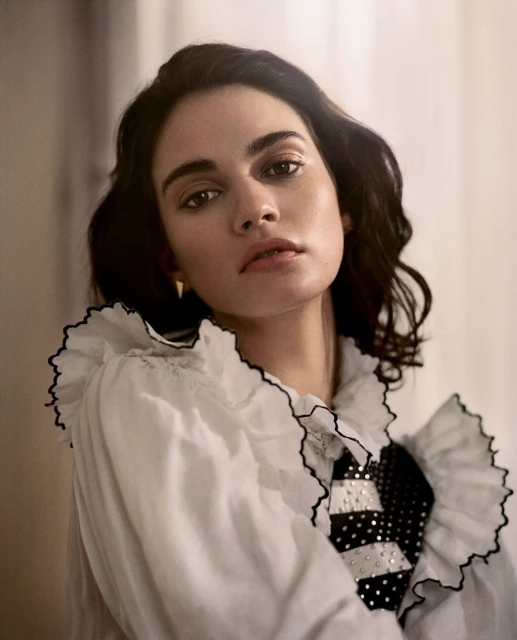 Portrait of a brunette woman wearing a white ruffled shirt with black trim, posing indoors in a brightly lit room.