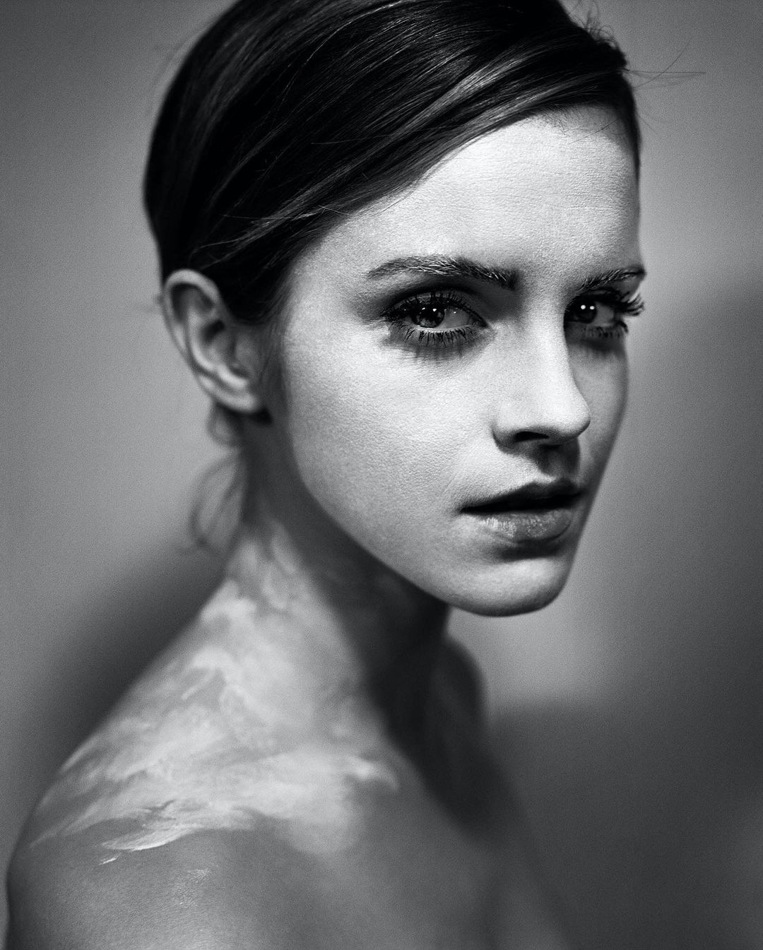 Monochrome portrait of a young fair-skinned woman gazing at the camera, set against a blurred background with atmospheric lighting effects.