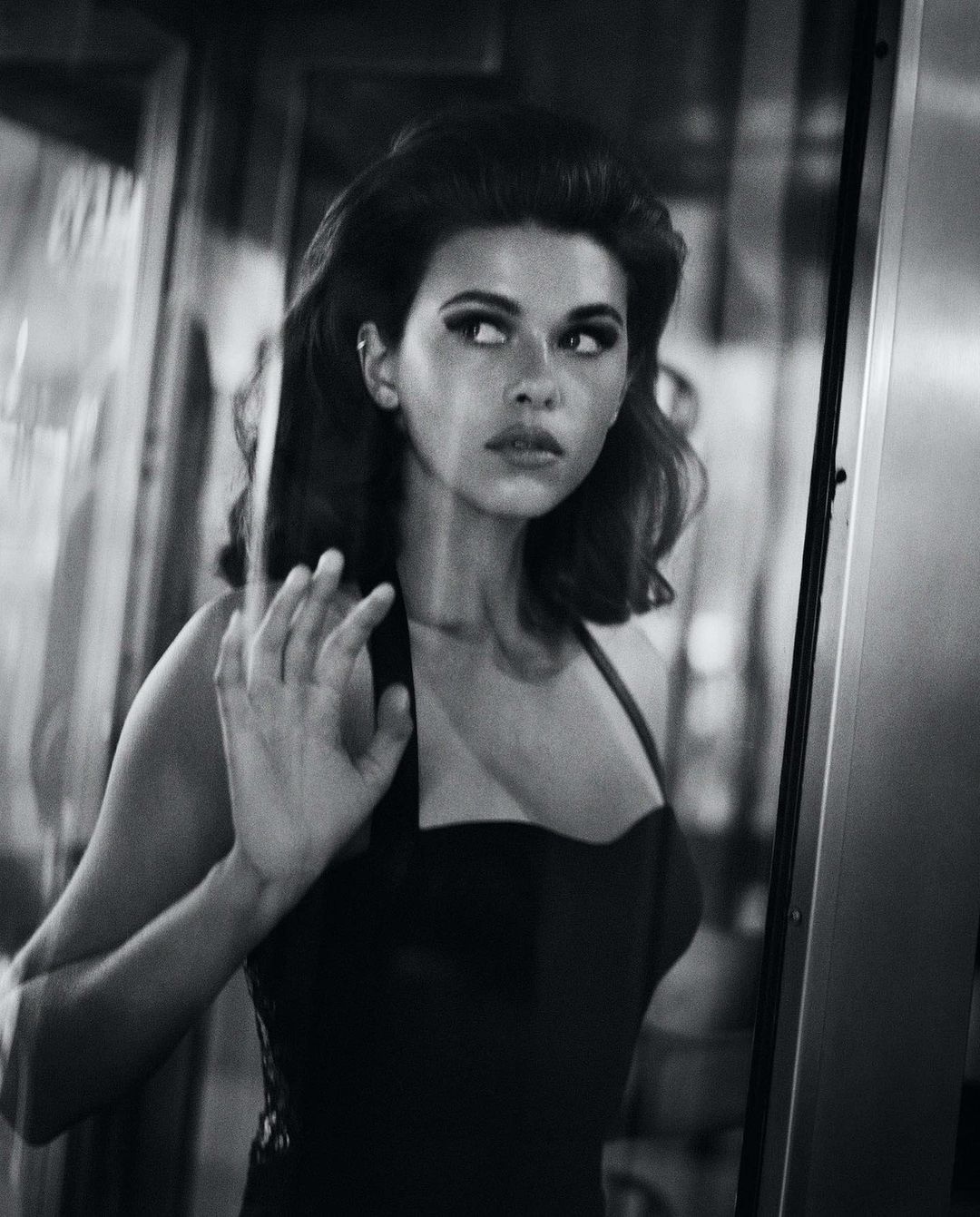 Black and white portrait of a woman looking sideways with her hand pressed against a glass door or window