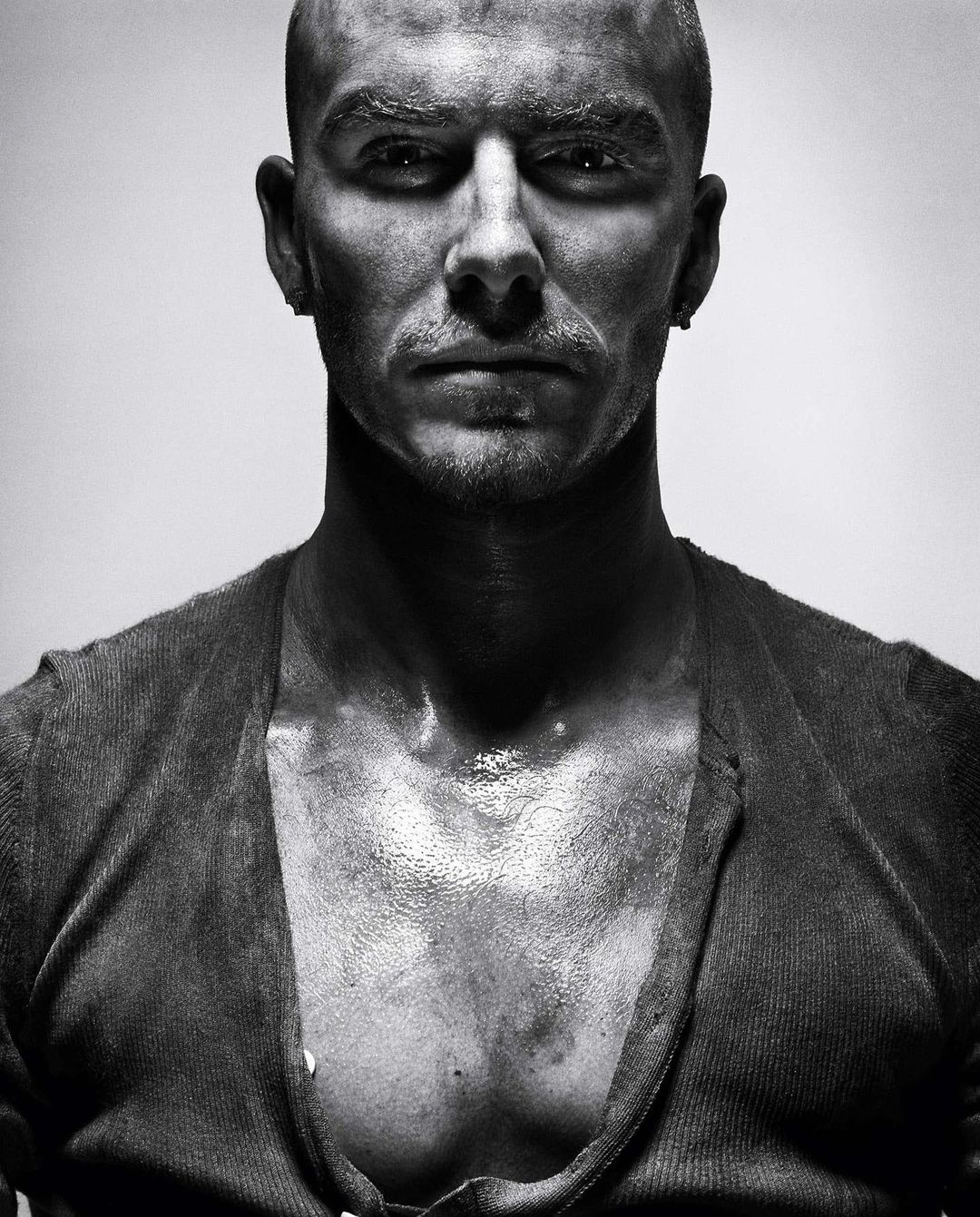 Black and white portrait of a bald adult male with an open cardigan, looking directly at the camera with a serious facial expression.