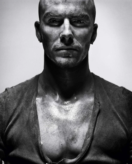 Black and white portrait of a bald adult male with an open cardigan, looking directly at the camera with a serious facial expression.
