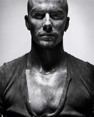 Black and white portrait of a bald adult male with an open cardigan, looking directly at the camera with a serious facial expression.