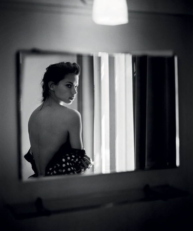 Black and white portrait of a woman looking over her shoulder in a mirror. Polka dot fabric, light fixture, and neutral background.