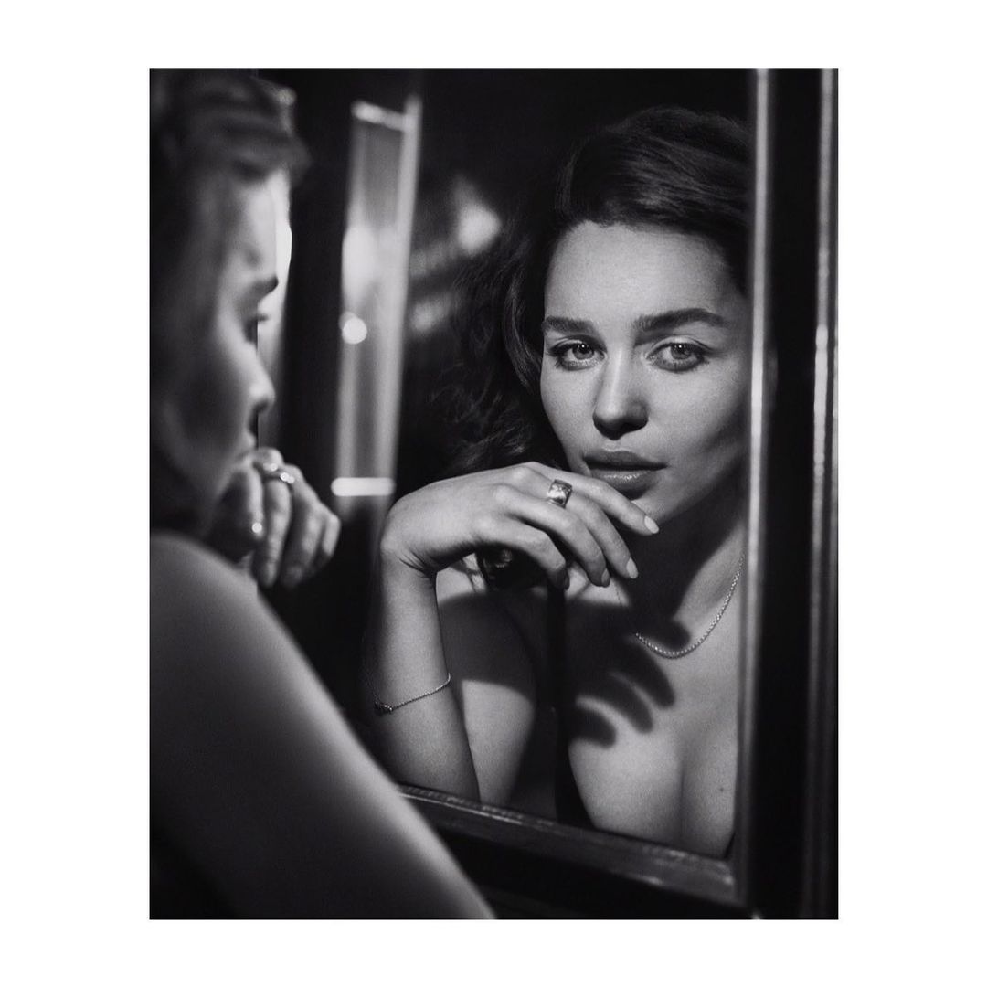 Black and white portrait of Emilia Clarke reflected in a mirror with her hand near her face wearing a ring.