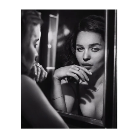 Black and white portrait of Emilia Clarke reflected in a mirror with her hand near her face wearing a ring.