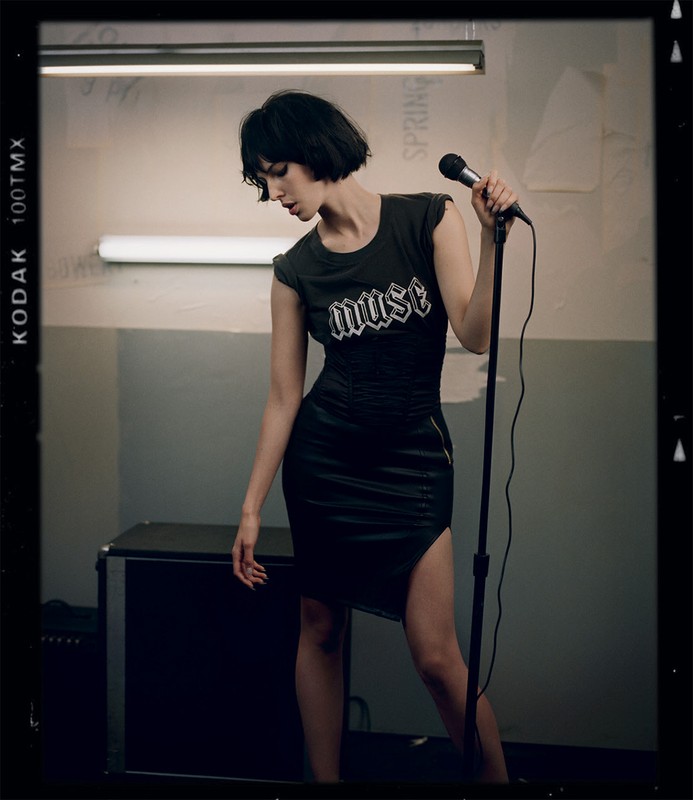 Adult female singer posing in a black dress with a microphone in an indoor setting. The photo is in portrait orientation.