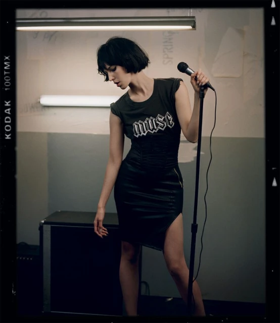 Adult female singer posing in a black dress with a microphone in an indoor setting. The photo is in portrait orientation.