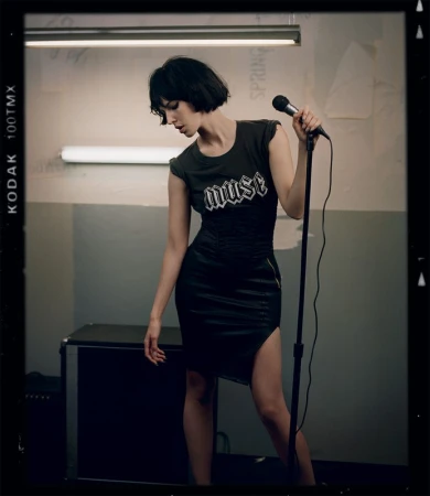 Adult female singer posing in a black dress with a microphone in an indoor setting. The photo is in portrait orientation.