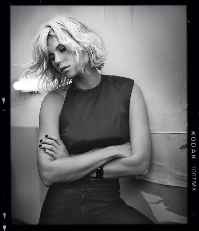 Black and white portrait of a blonde woman with short wavy hair crossing her arms by photographer Vincent Peters