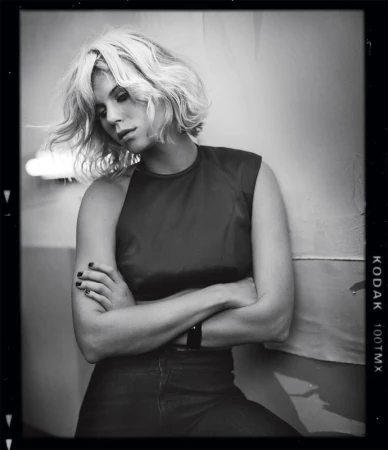 Black and white portrait of a blonde woman with short wavy hair crossing her arms by photographer Vincent Peters