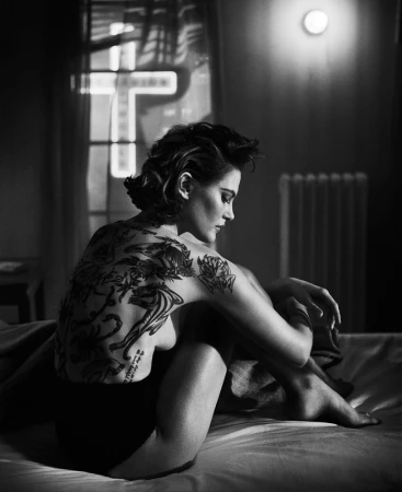 Monochrome portrait of tattooed woman seated on a bed by Vincent Peters