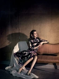 Woman in patterned dress seated on a vintage sofa against a textured wall photographed by Vincent Peters.
