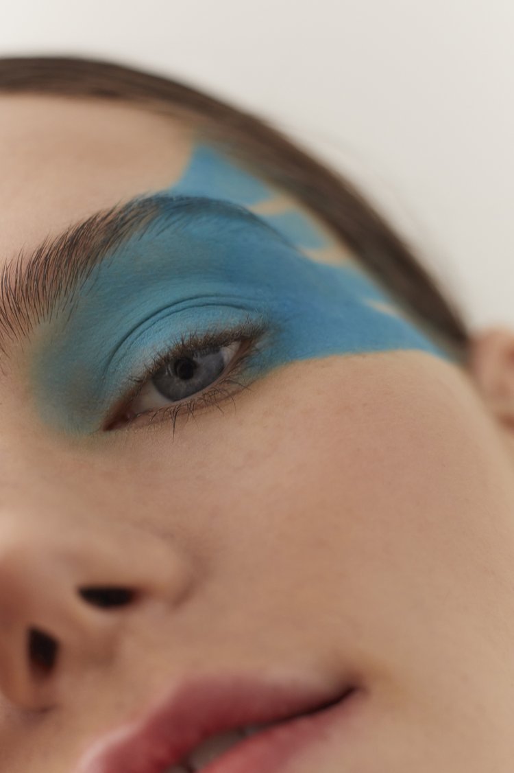 Close-up portrait of a woman featuring bold blue eyeshadow swept across her brow and eyelid, styled by hair stylist Vivi.