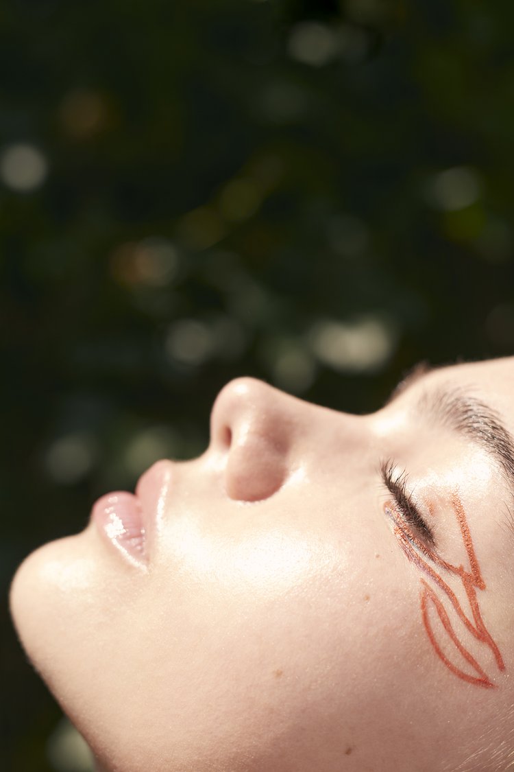 Close-up shot of a person's face in an outdoor setting with skin art around the eye, emphasizing light skin and natural light.