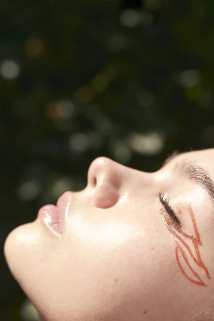 Close-up shot of a person's face in an outdoor setting with skin art around the eye, emphasizing light skin and natural light.