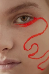 Close-up beauty portrait of a person with a bold red graphic eyeliner design swirling across the cheek and eye.