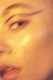 Close-up beauty portrait of a person with warm golden lighting, winged eyeliner, and motion-blurred facial features.