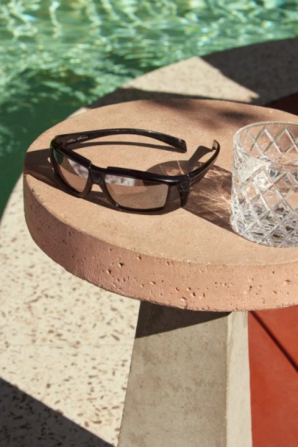 Sunglasses and a glass sit on a concrete side table next to a pool, capturing a bright, sunny day aesthetic.