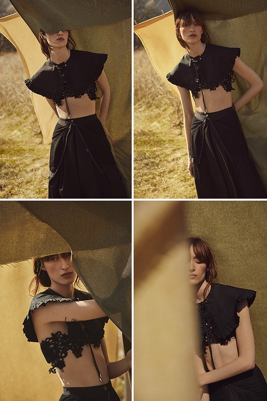 Fashionable woman in black two-piece outfit with lace detailing posing outdoors on a sunny day with cloth backdrop.