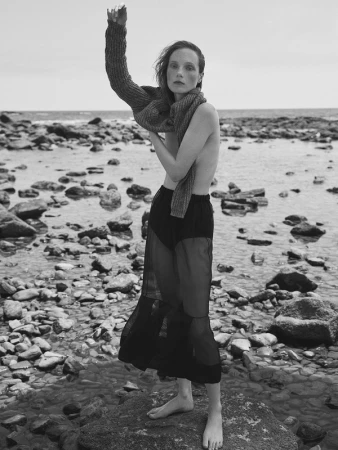 Monochrome fashion portrait of a model standing on a rocky shore wearing a knit sweater and dark sheer skirt by Williams + Hirakawa.