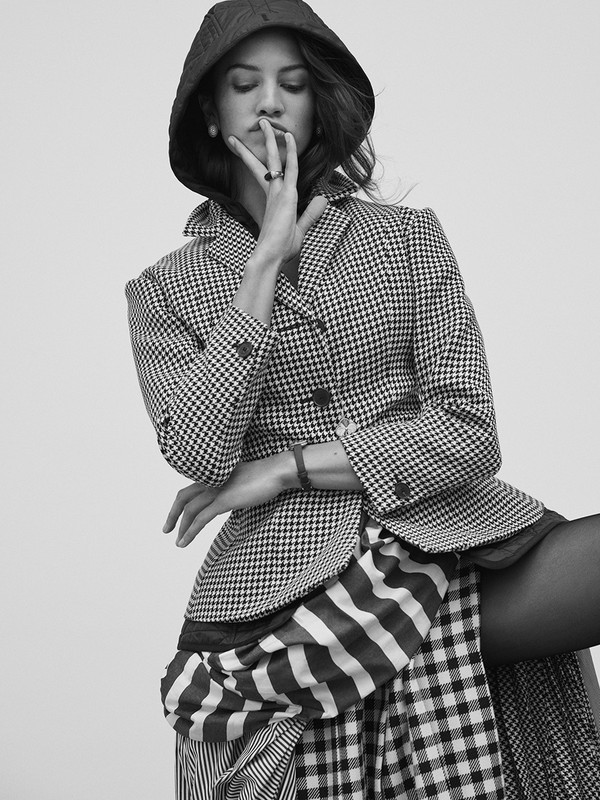 Monochrome portrait of a woman in a patterned blazer, posing elegantly with her hand near her face, creating a stylish and refined studio shot.