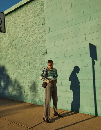 Woman in a striped sweater and grey jeans standing in front of a green concrete block wall