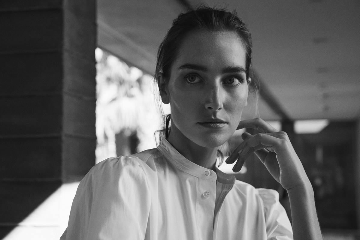 Black and white portrait of an adult woman wearing a white blouse, looking directly at the camera in an indoor setting.