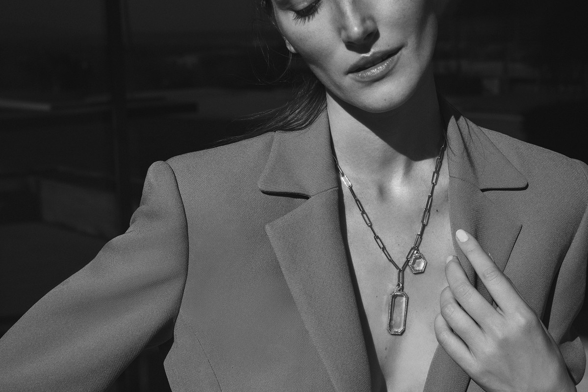 Monochrome fashion portrait of a woman wearing a blazer and statement jewelry. Necklace with two large pendant charms.