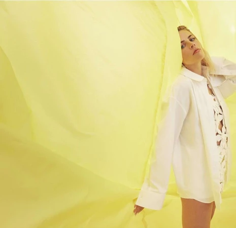 Woman in white shirt posing against a bright yellow draped fabric backdrop