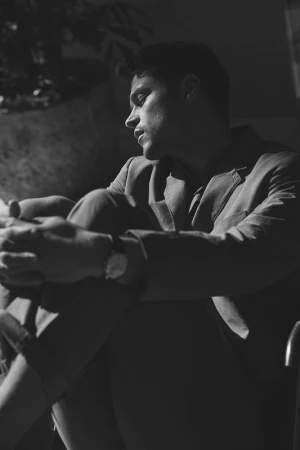 Monochrome portrait of a man in a blazer seated with his knees drawn up, photographed by Williams + Hirakawa.
