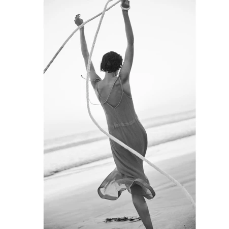 Monochrome image of a woman in a long dress holding ropes on a sandy beach