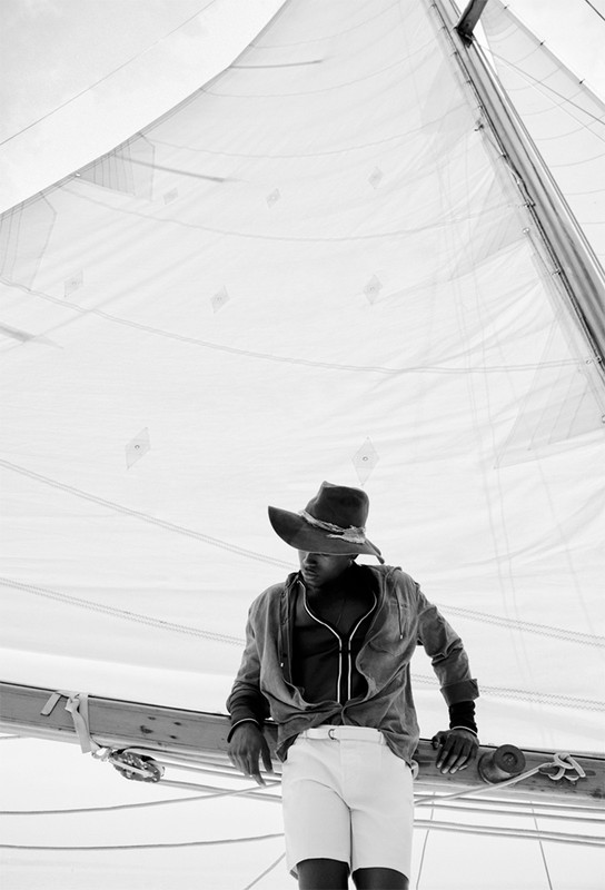 Monochrome portrait of a man in a hat on a sailboat, showcasing the interplay of light and shadow on the sails and the man's attire.