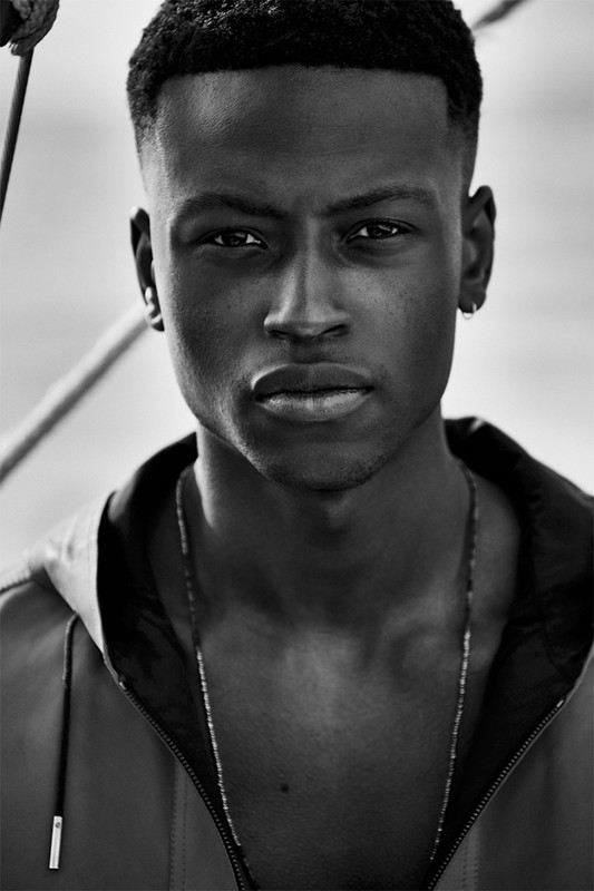 Close-up black and white portrait of a young Black man wearing a hooded jacket and thin necklace by Williams plus Hirakawa.