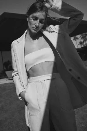 Monochrome portrait of a woman wearing a white bandeau top, trousers, and a blazer by photographers Williams + Hirakawa.