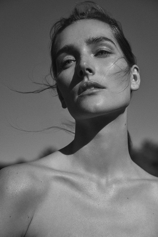 Monochrome portrait of a woman looking upward with hair gently blowing in the wind against an outdoor background