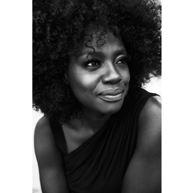 Striking black-and-white portrait of a smiling African-American woman with natural hair, wearing a draped top, looking off to the side.