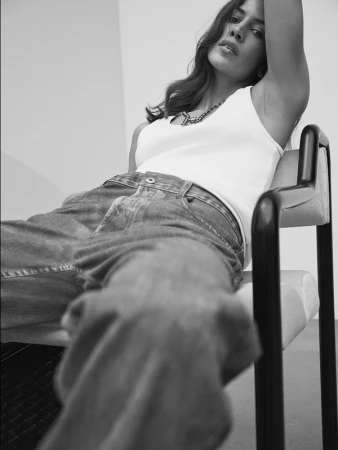 Model wearing a white tank top and baggy jeans seated in a modern armchair photographed by Williams + Hirakawa.