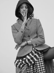 Model in hooded houndstooth jacket and striped skirt posing against a white background by Williams + Hirakawa.