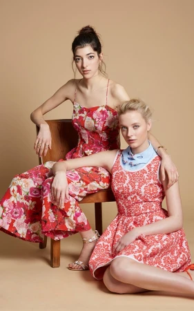 Two female models in red patterned dresses posing together with a wooden chair in a studio setting