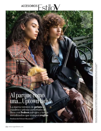 Two models seated on a park bench, one wearing a plaid fringe jacket and the other a black leather jacket with a black handbag.