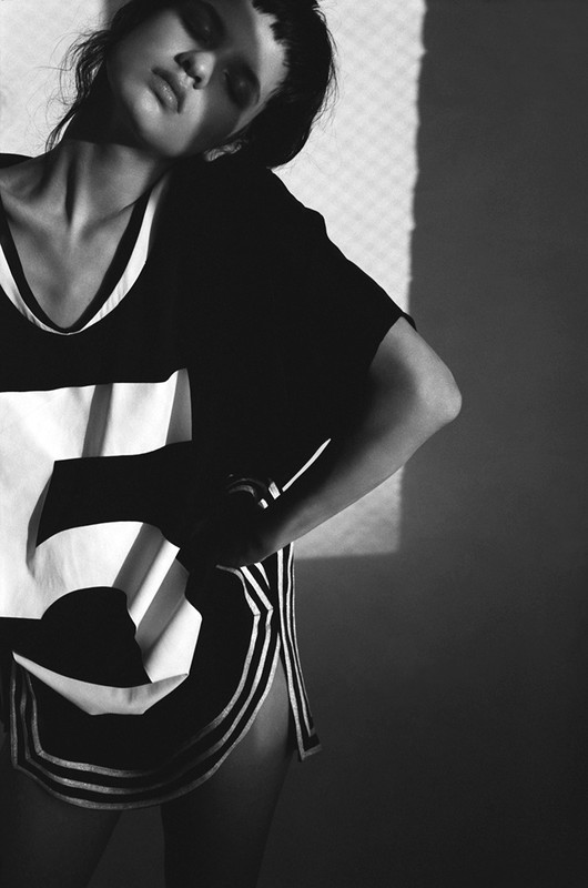 Monochrome fashion shot of a woman posing in a sports jersey with the number five, contrasted by sharp shadow and a net background.
