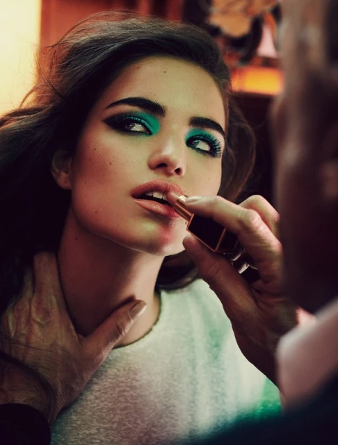 Close-up of a model getting her makeup done with vibrant turquoise eyeshadow and lipstick applied by a makeup artist.