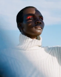 Black woman with striking red eyeshadow wearing a white turtleneck sweater against a clear sky background