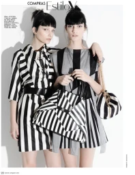Two female models in black and white striped dresses posing together against a plain white background holding patterned handbags.