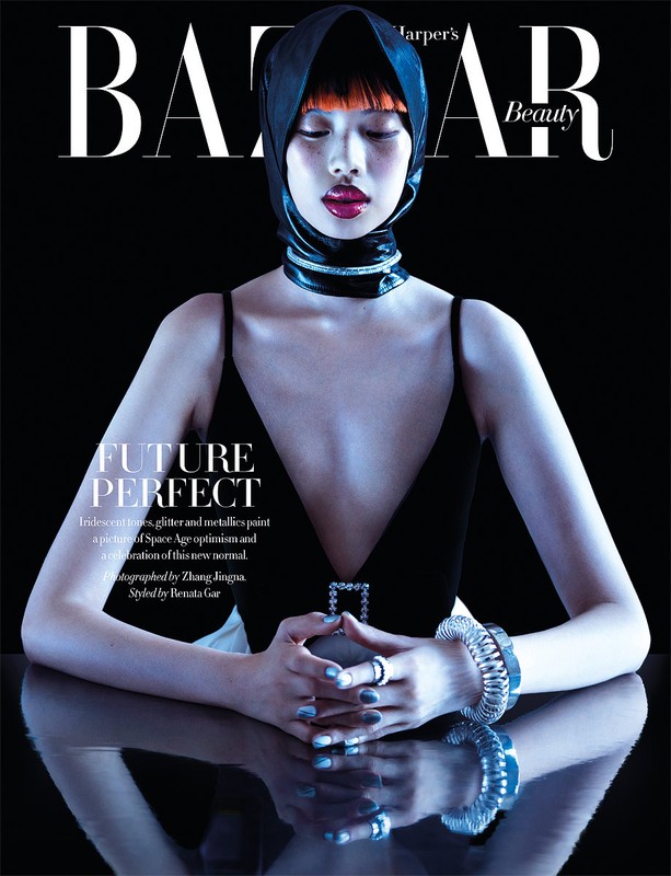 Magazine cover featuring a person with a head covering, wearing a black dress and jewelry, gazing down on a reflective surface.
